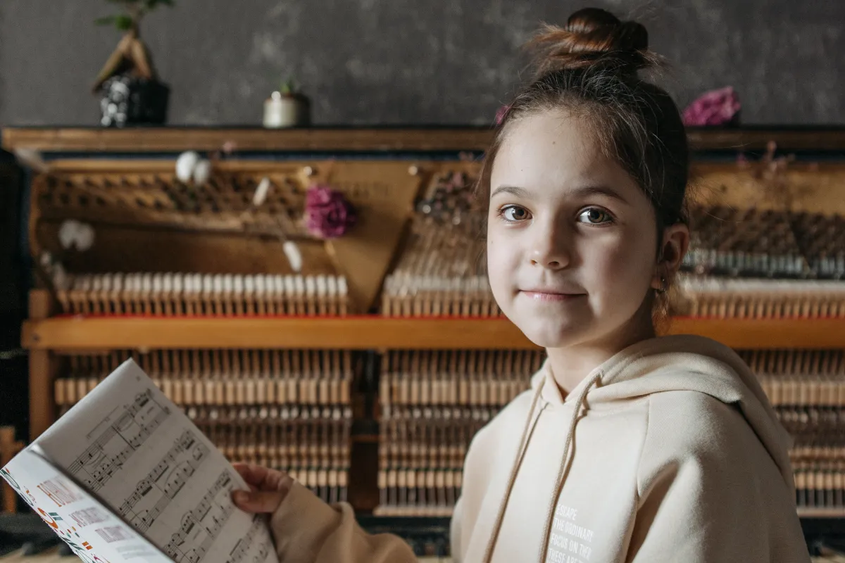 Two children playing an upright piano together, one focusing on the lower keys and the other on the higher ones. Both kids are smiling, engaged in playing, in a cozy room with warm lighting. The scene highlights the joy of collaborative music-making.