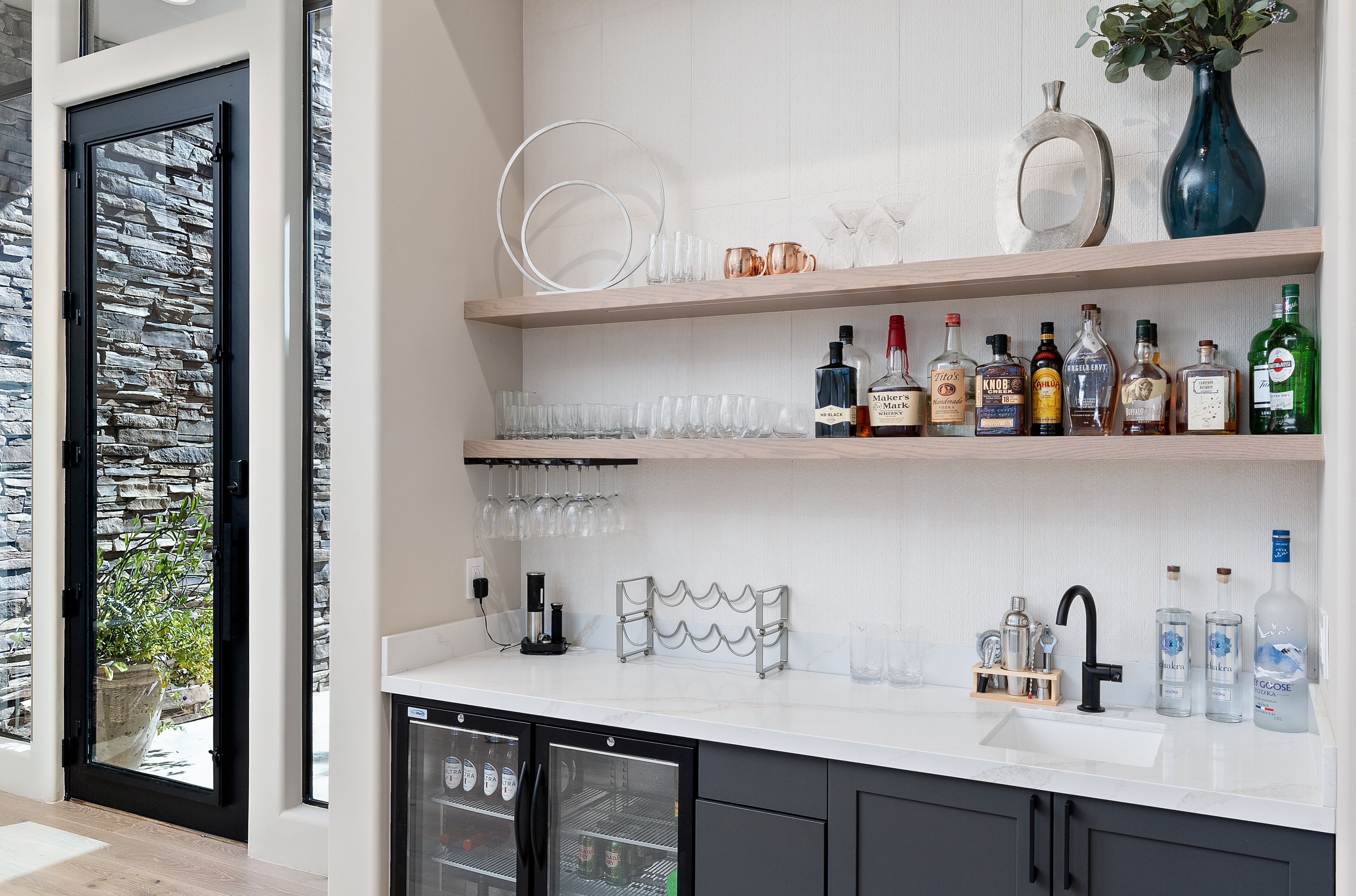 Luxury home entry with custom wet bar, ring chandelier, black-frame floor-to-ceiling windows, and natural stone facade — N&M Home Services, Desert Mountain AZ