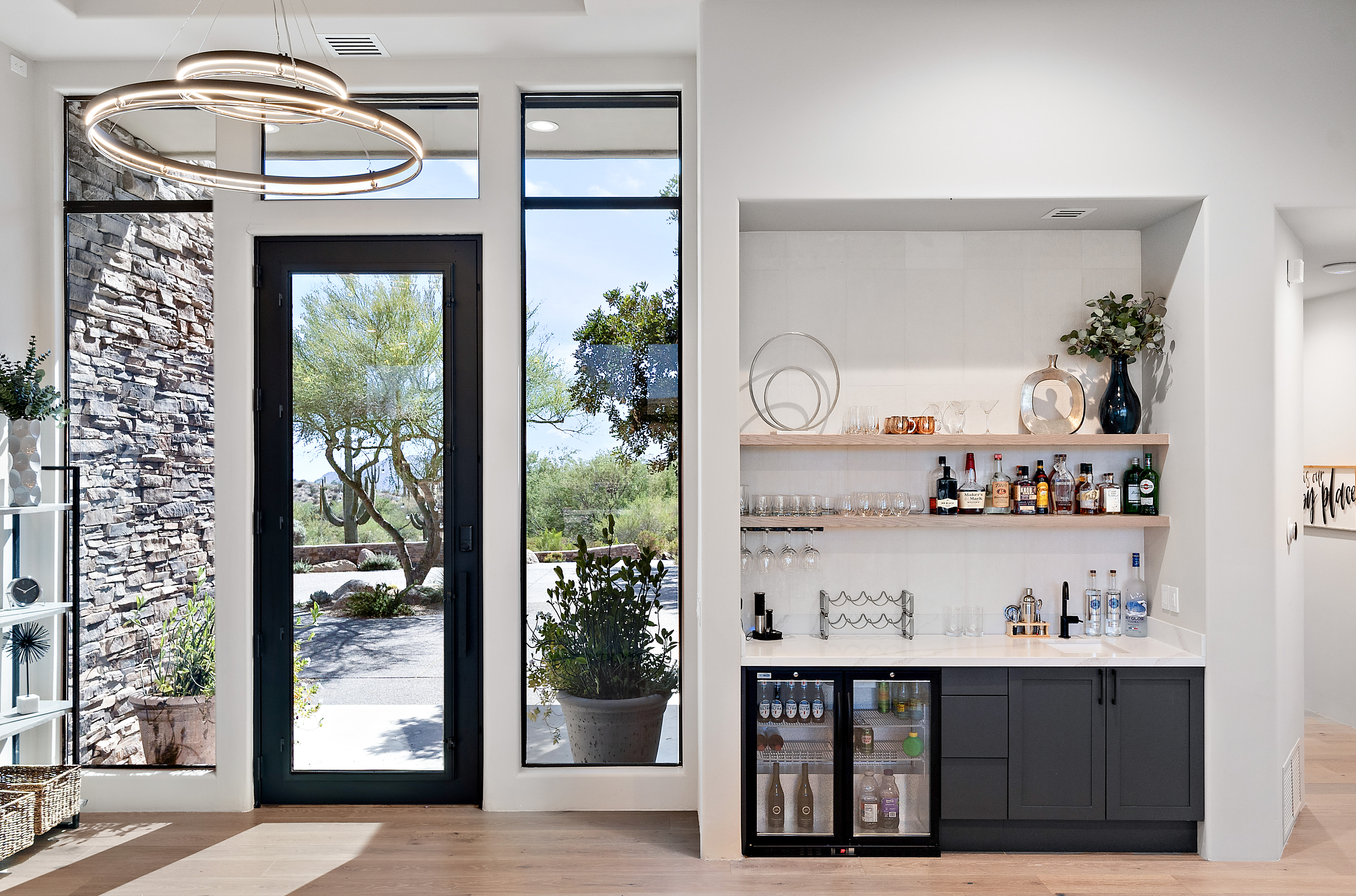 Luxury home entry with custom wet bar, ring chandelier, black-frame floor-to-ceiling windows, and natural stone facade — N&M Home Services, Desert Mountain AZ