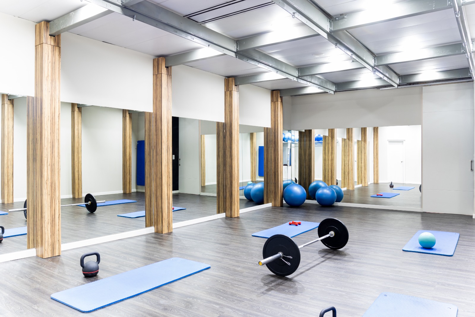 Open gym studio with wall-to-wall gym mirrors, blue workout mats, barbells, and exercise equipment for floor work | Creoglass