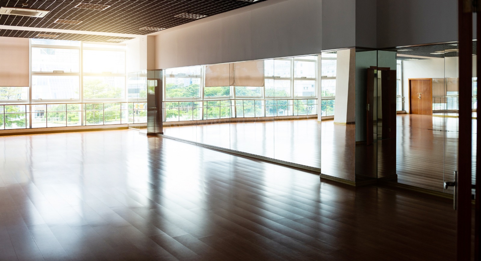 Commercial-grade exercise mirror with a seamless, floor-level installation, reflecting the light and providing an open feel in a spacious multi-purpose studio. | Creoglass