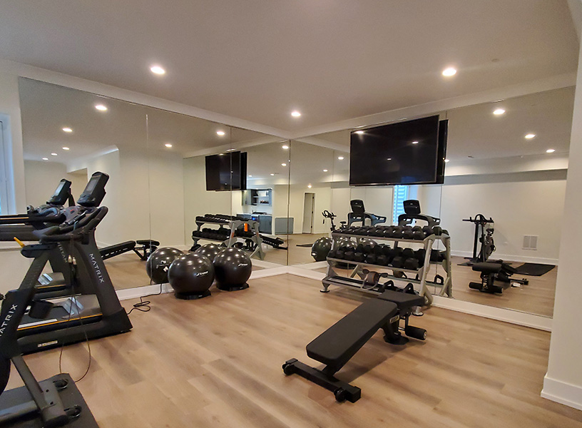 Home gym setup with large, floor-to-ceiling gym miror, dumbbell rack, weight bench, and cardio machines | Creoglass