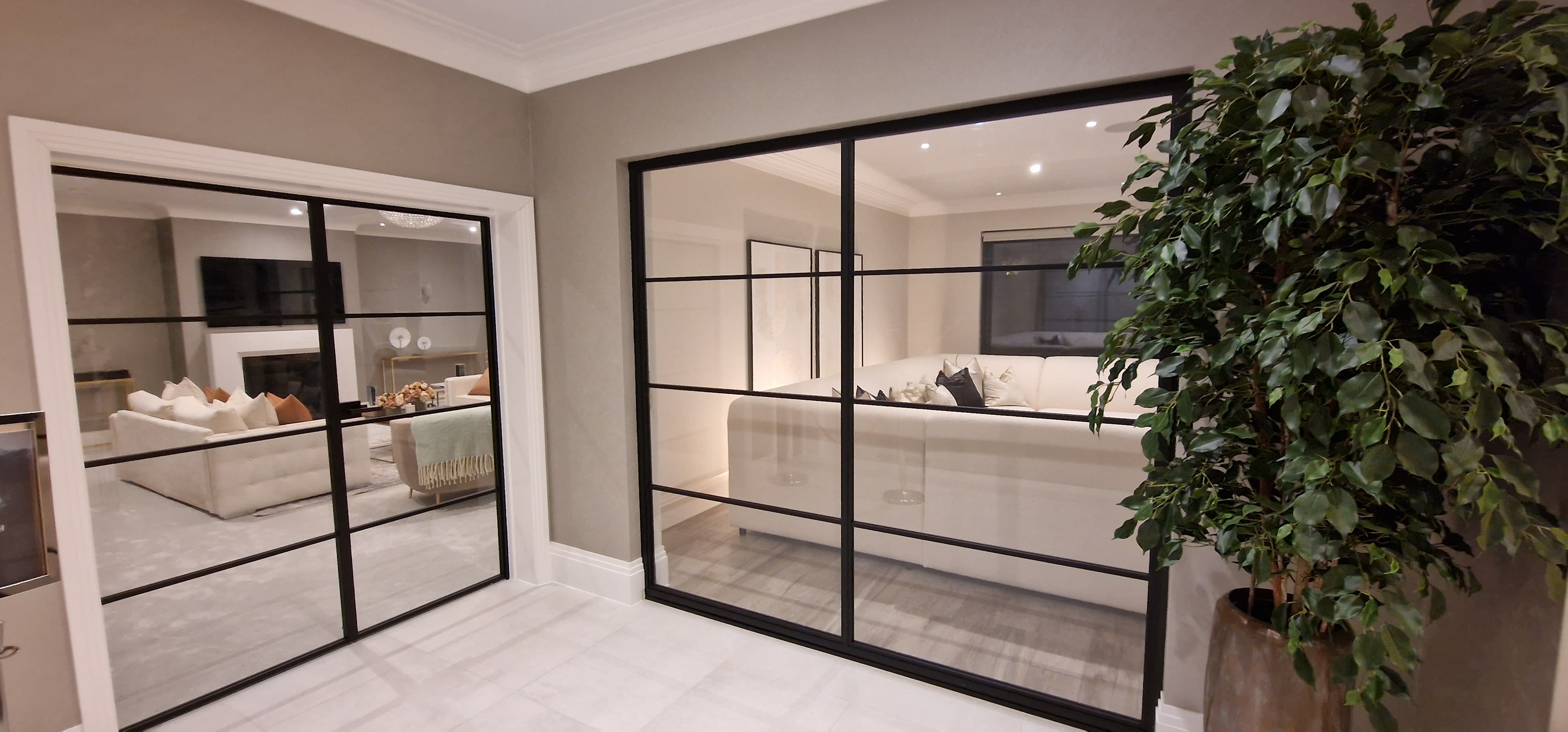 Fixed glass partition screen and a single hinged door with black frames looking into a living room. | Creoglass