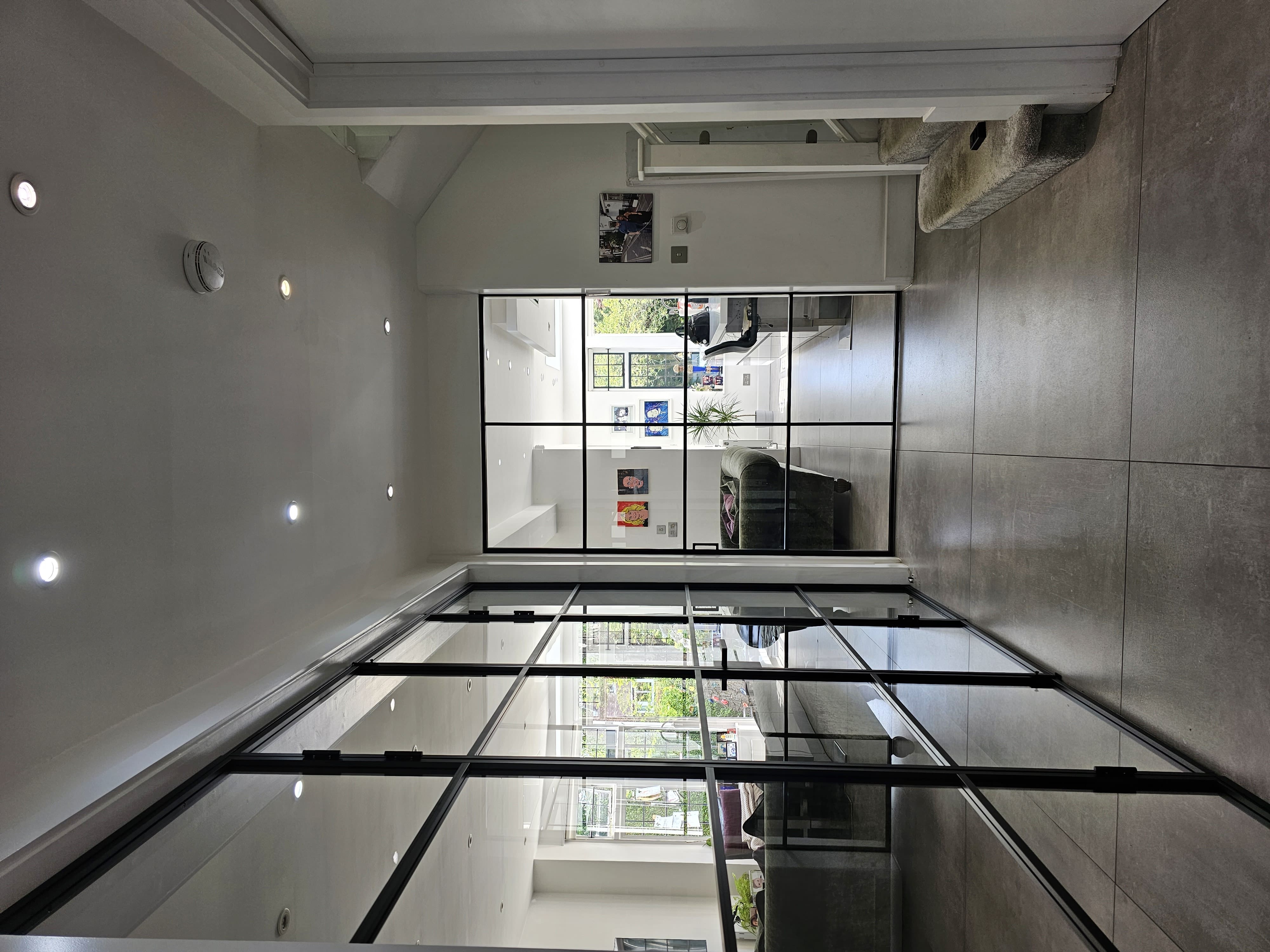 Long black-framed fixed glass screen and a single door at the end of a modern hallway. | Creoglass