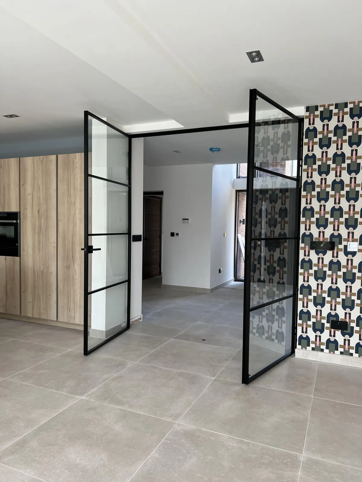 Single black-framed glass door surrounded by fixed glass panels on a herringbone floor. | Creoglass