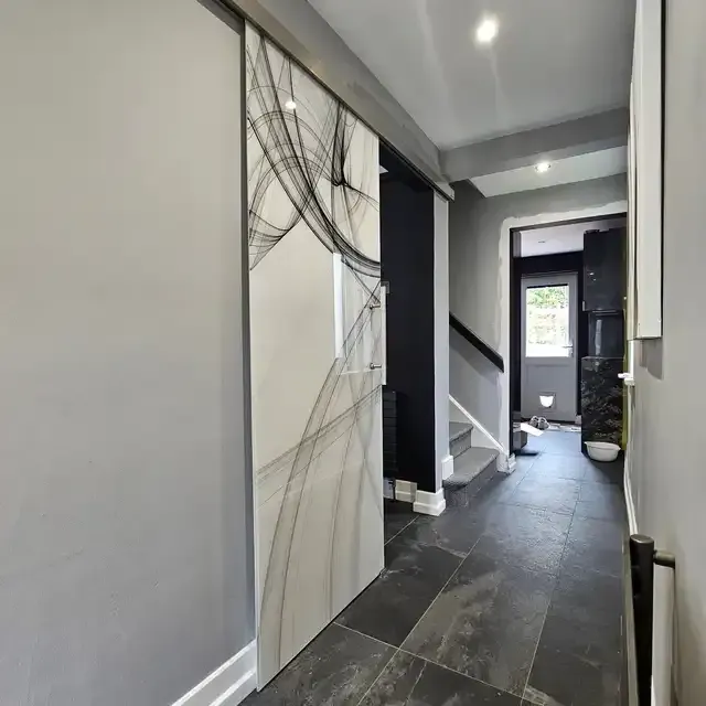 Single frameless sliding glass door with a custom abstract design in a gray hallway. | Creoglass
