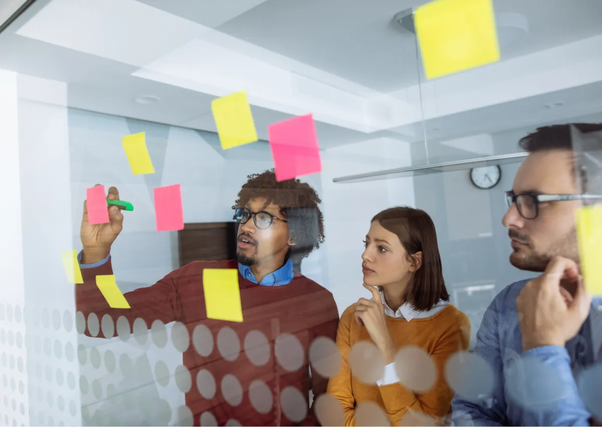 Equipe organizando tarefas e planejamento estratégico utilizando blocos de notas adesivas em painel de vidro