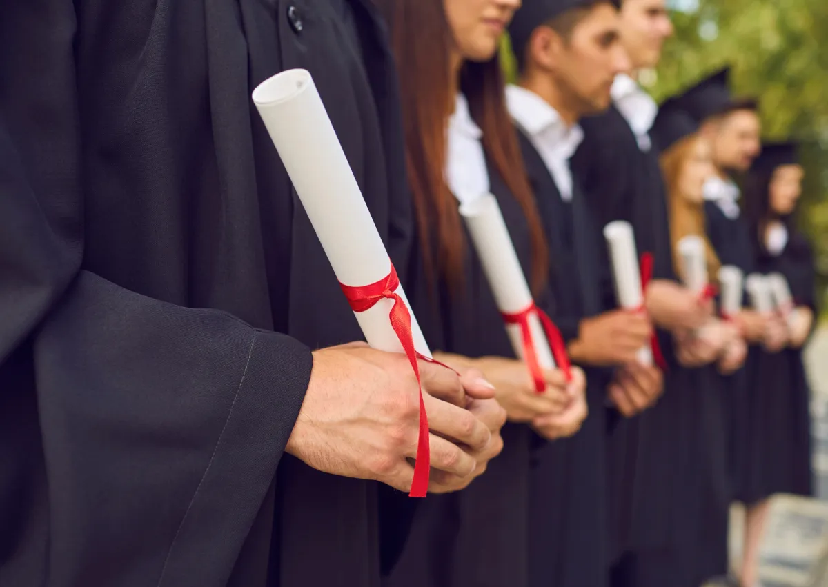 Estudantes formandos vestindo bata e capelo segurando diplomas em cerimônia de graduação