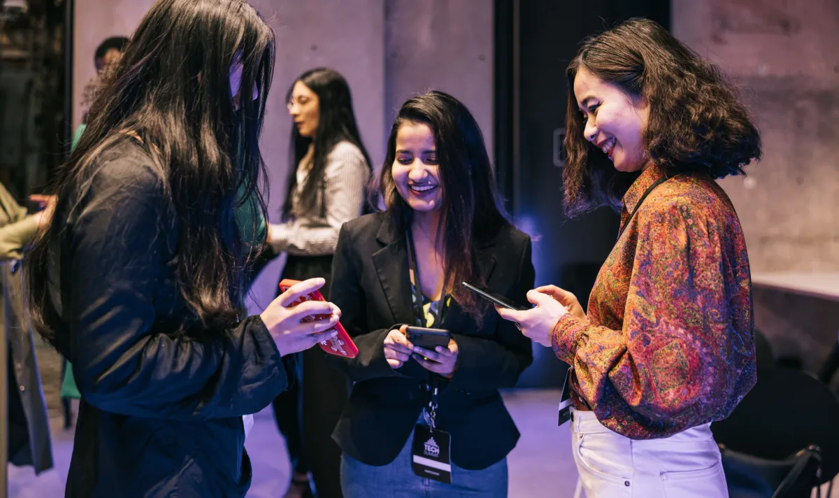 Equipe de credenciamento e recepção de eventos sorrindo enquanto interage com participantes usando crachás e tablets