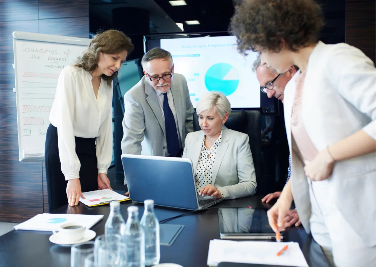 Equipe profissional reunida em mesa de reunião analisando gráficos no notebook