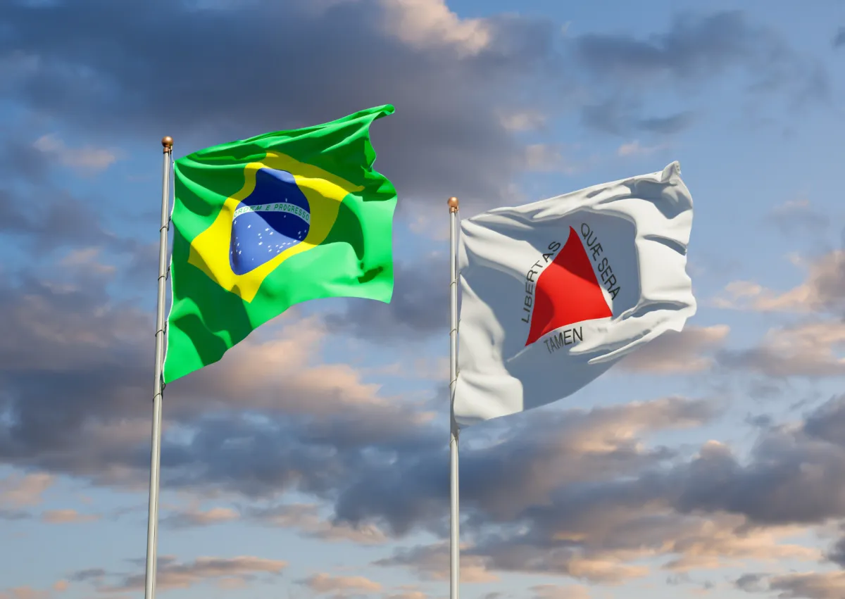 Bandeira do Brasil e bandeira do estado de Minas Gerais hasteadas lado a lado contra céu nublado ao entardecer