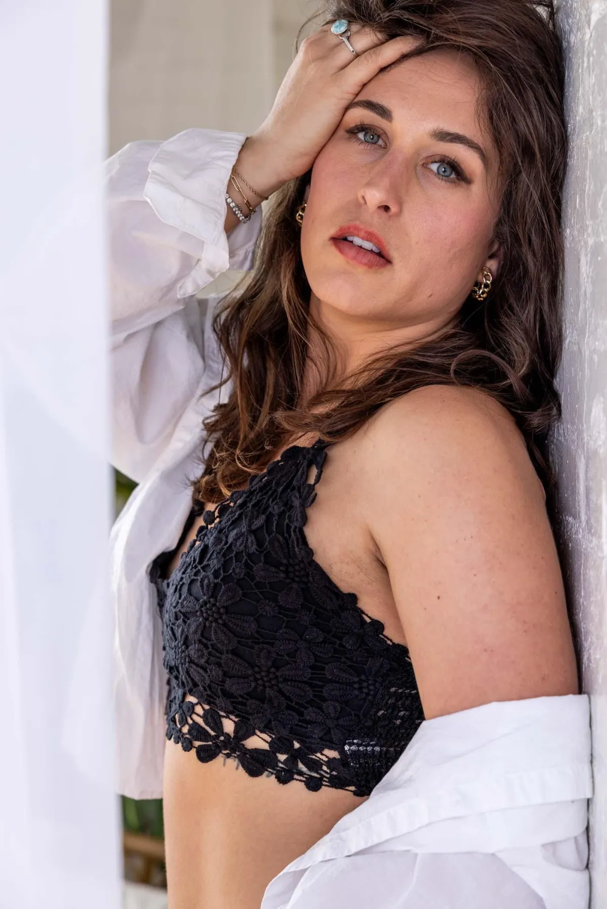 Grand Rapids boudoir photography - middle aged woman leaning on a wall wearing a black bralet and loose white button up shirt.