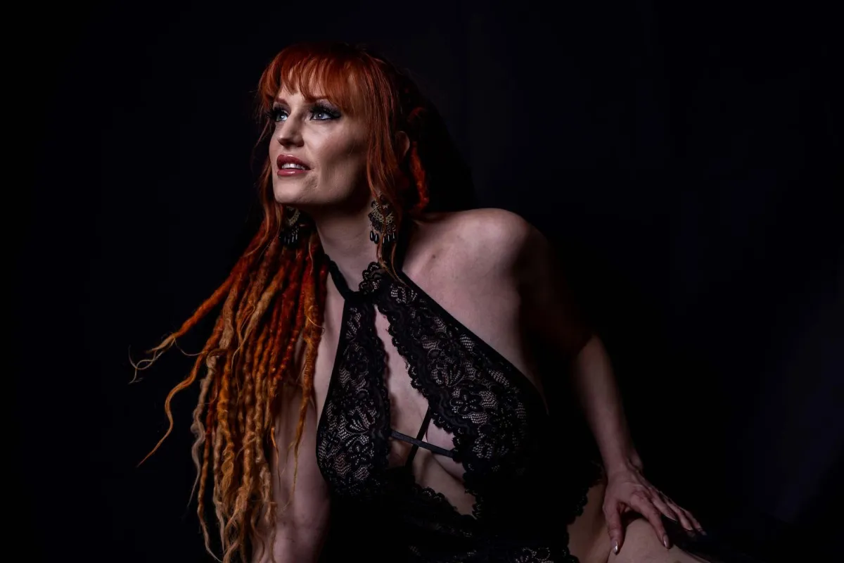 Grand Rapids boudoir photography - dark and moody, entirely black background, woman with long dreads wearing a black lace body suit.