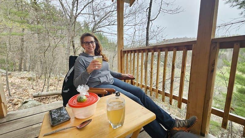 Guest relaxing with a glass of wine on the deck of Cliffside Camp Shelter in Quebec’s Outaouais region, overlooking forest views.