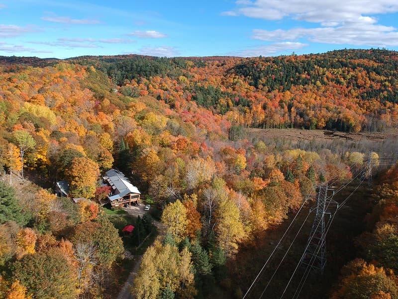 Drone view of The Ark property in the Outaouais, Quebec, surrounded by peak fall colours in the forested hills