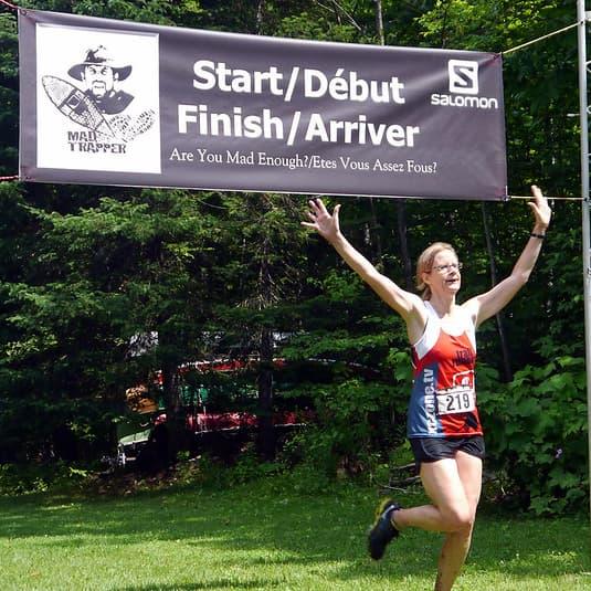 Runner celebrating at the finish line of the Mad Trapper trail race at the Off Grid Ark in Quebec, part of Canada’s longest-running trail and snowshoe race series.