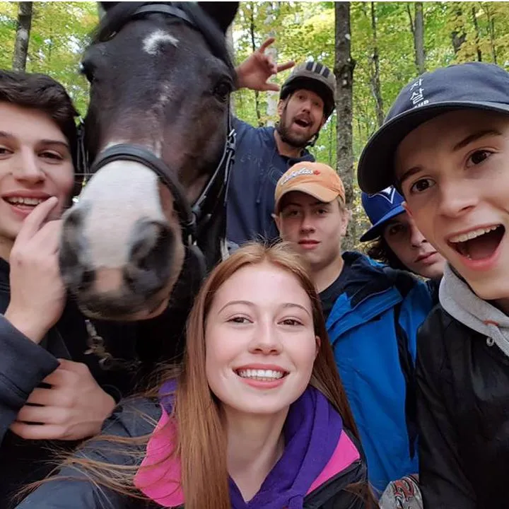 Group of participants with a horse during the Mantracker activity at the Off Grid Ark in Quebec, where players use map and compass while being chased on horseback.