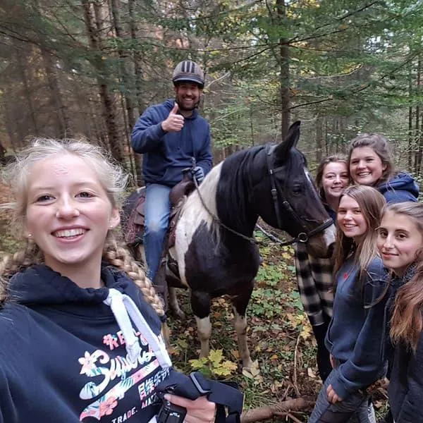 Group of smiling participants with guide on horseback during Mantracker adventure at The Off Grid Ark in Quebec forest.