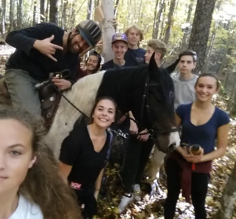 Group of young adults posing with horseback guide in forest during Mantracker challenge at The Off Grid Ark, Quebec.