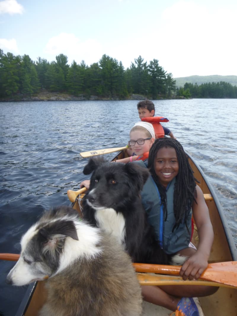 youth canoeing with life jackets and dogs on the Gatineau River during outdoor adventure camp at The Off Grid Ark in Western Quebec