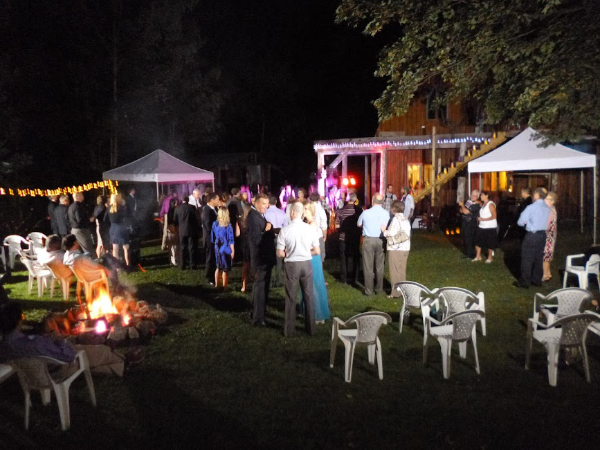 Evening wedding celebration with guests gathered outdoors around a bonfire and music"