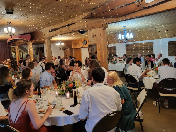 Wedding guests seated at tables during an indoor reception in a wood-framed space
