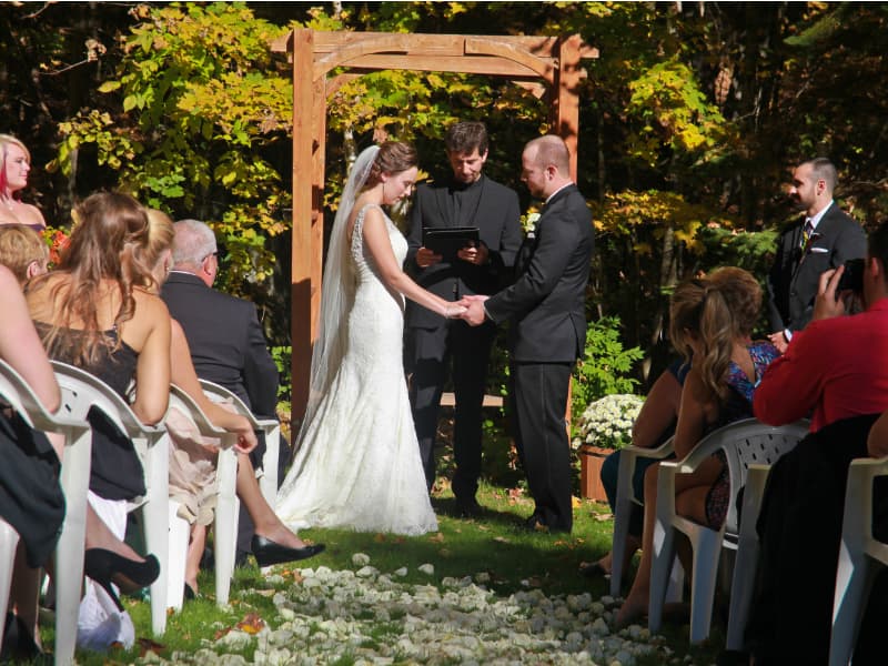 Outdoor wedding ceremony at The Off Grid Ark near Ottawa–Gatineau, with bride and groom exchanging vows under a wooden arbor in a forest setting.