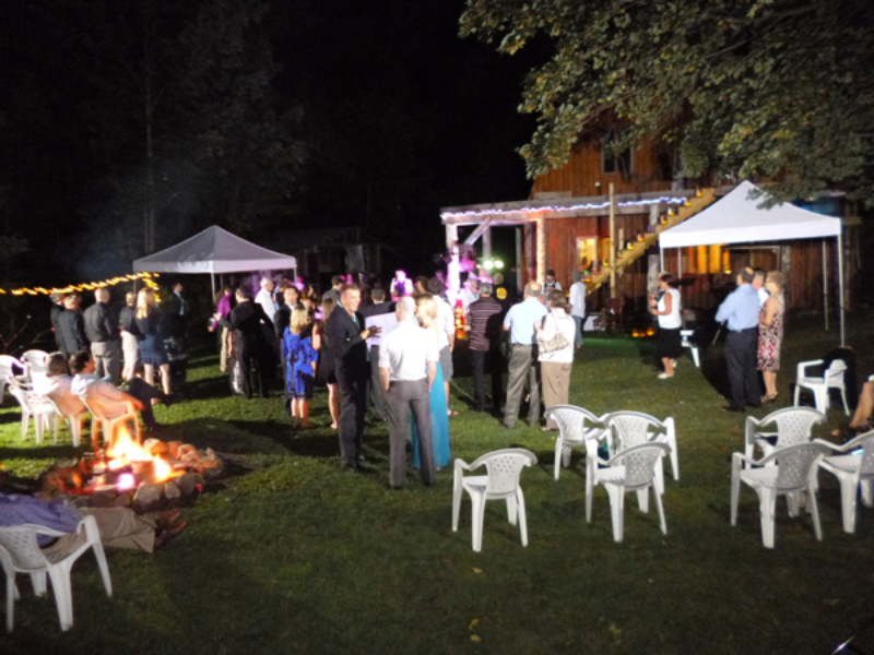 Outdoor evening wedding reception at The Off Grid Ark with string lights, a bonfire, and guests gathering in the forest near Ottawa–Gatineau.