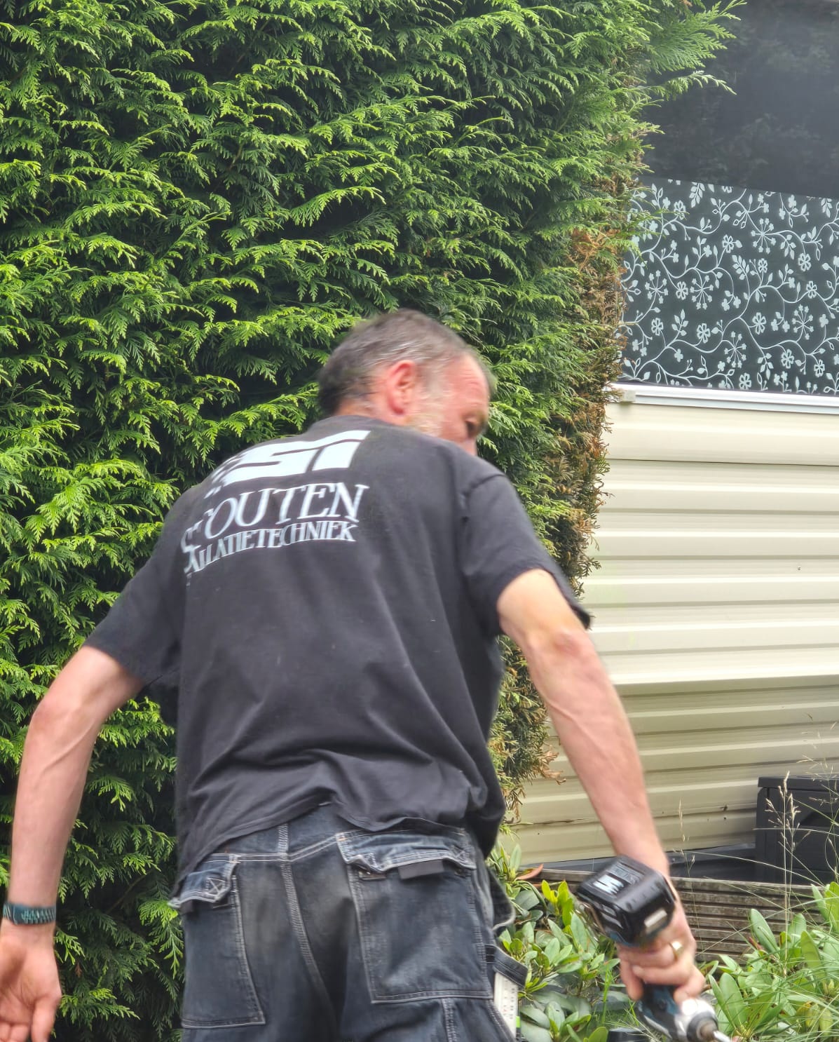 Team van Stouten Installatietechniek poseert voor hun bedrijfsbus, diverse leeftijden en achtergronden, allemaal in nette bedrijfskleding, buiten op locatie, heldere dag, vriendelijke uitstraling.