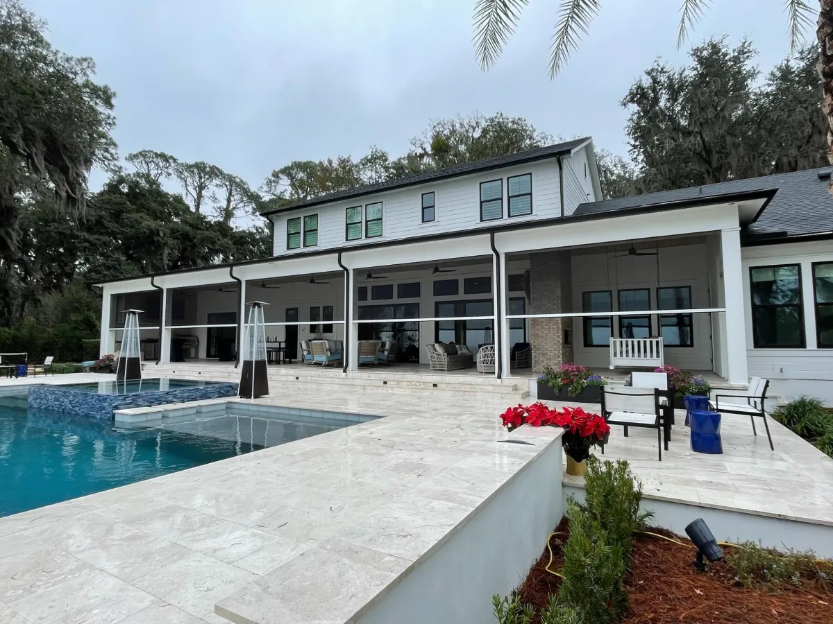 Project Gallery — Specified, Installed, Documented. Luxury residential home with professionally certified retractable screen enclosure along a poolside patio, featuring white modern architecture, travertine pool deck, and lush tropical landscaping — written into construction documents by a certified team
