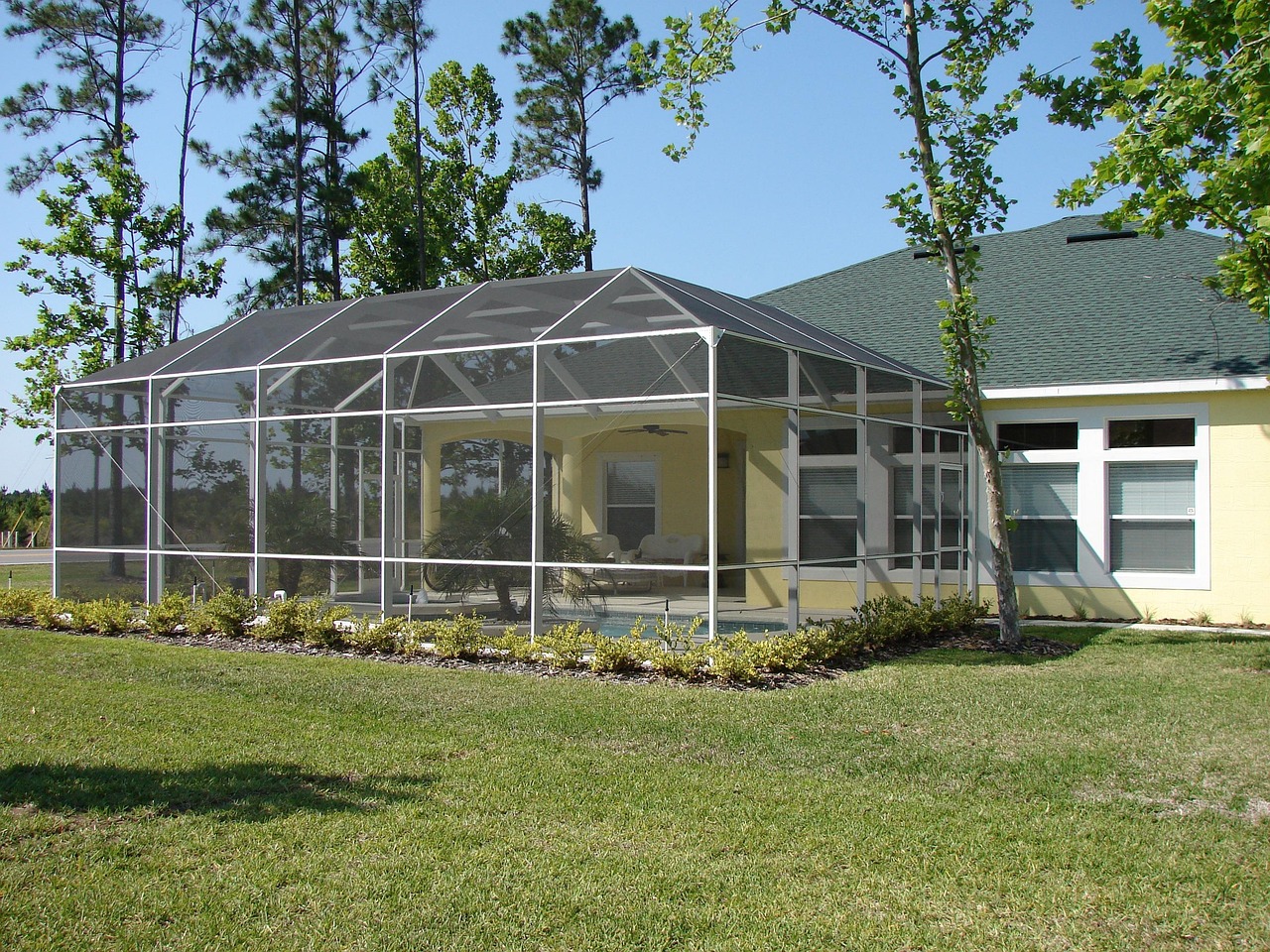 Screened-in patio enclosure attached to backyard home with aluminum frame and mesh panels.
