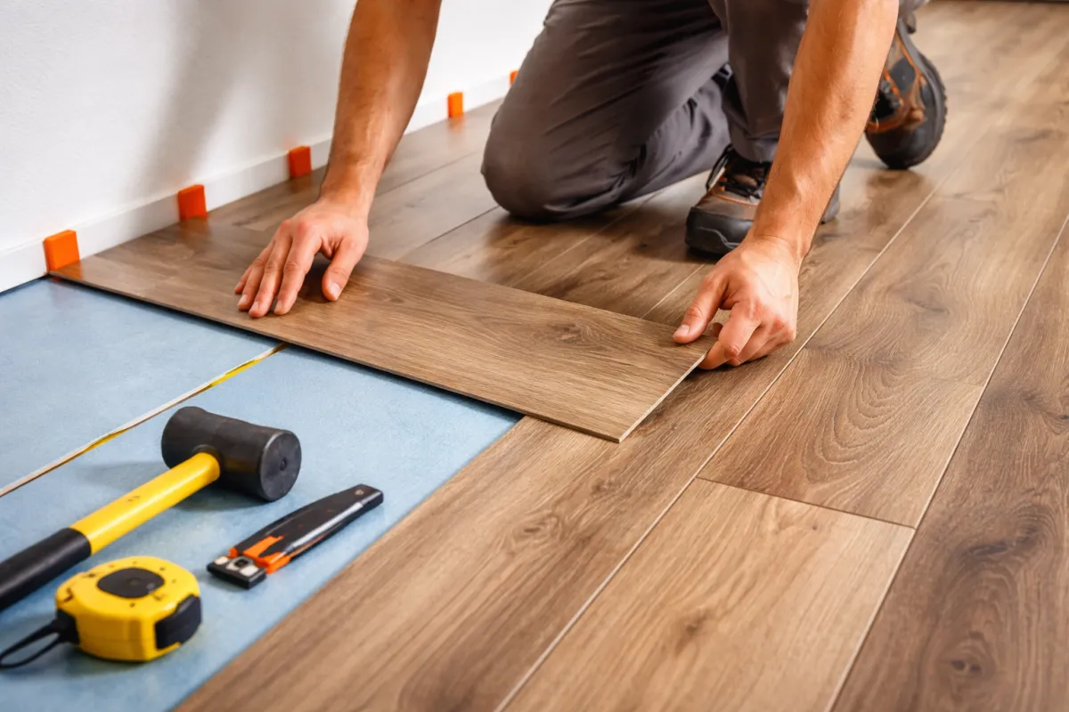 Handyman installing wood laminate flooring planks with tools during home floor installation