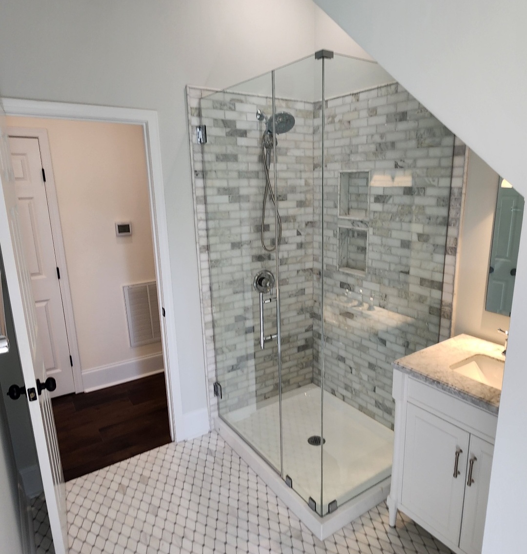 Modern bathroom renovation featuring a glass walk-in shower with marble subway tile, built-in shower niches, hexagon tile floor, and white vanity under a sloped ceiling.