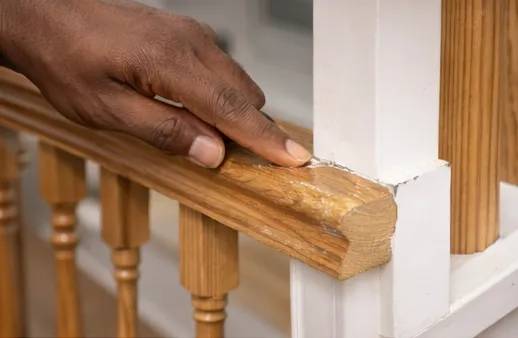 Handyman inspecting damaged stair railing and chipped wood trim during interior staircase repair