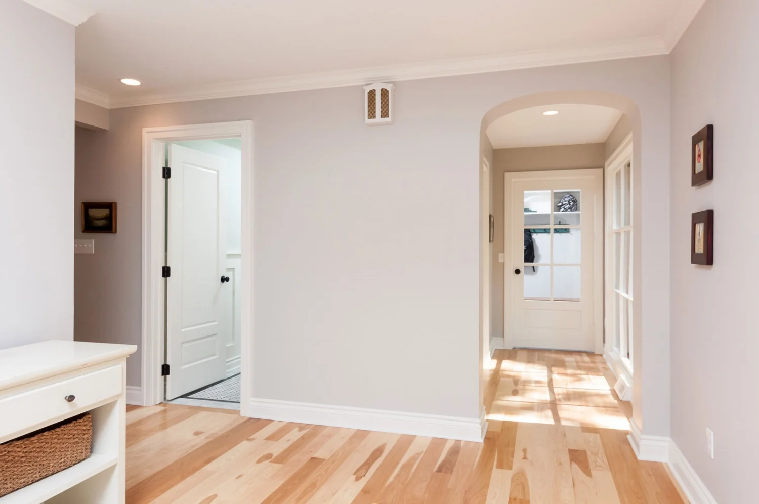 Bright home interior hallway with light hardwood floors, white trim, arched doorway, and soft gray walls.