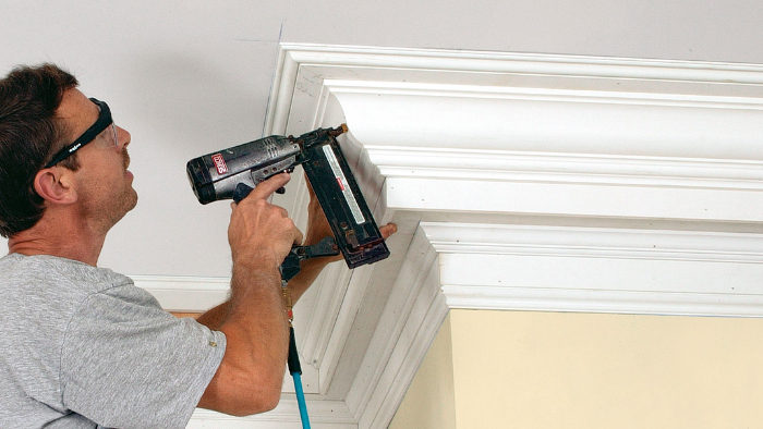 Carpenter installing decorative crown molding using a nail gun during interior home trim work.