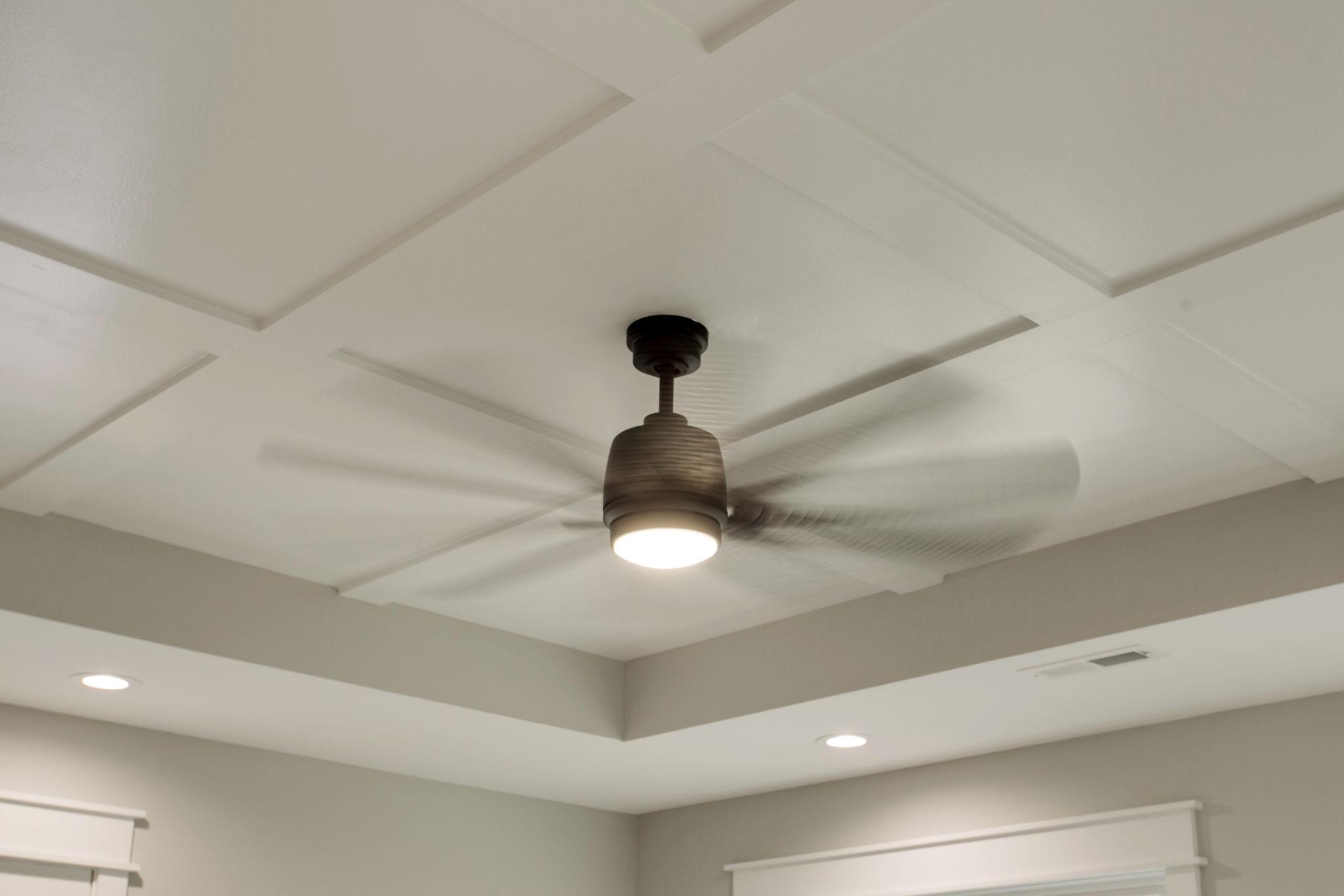 Modern ceiling fan with integrated light installed on coffered ceiling in residential living space.