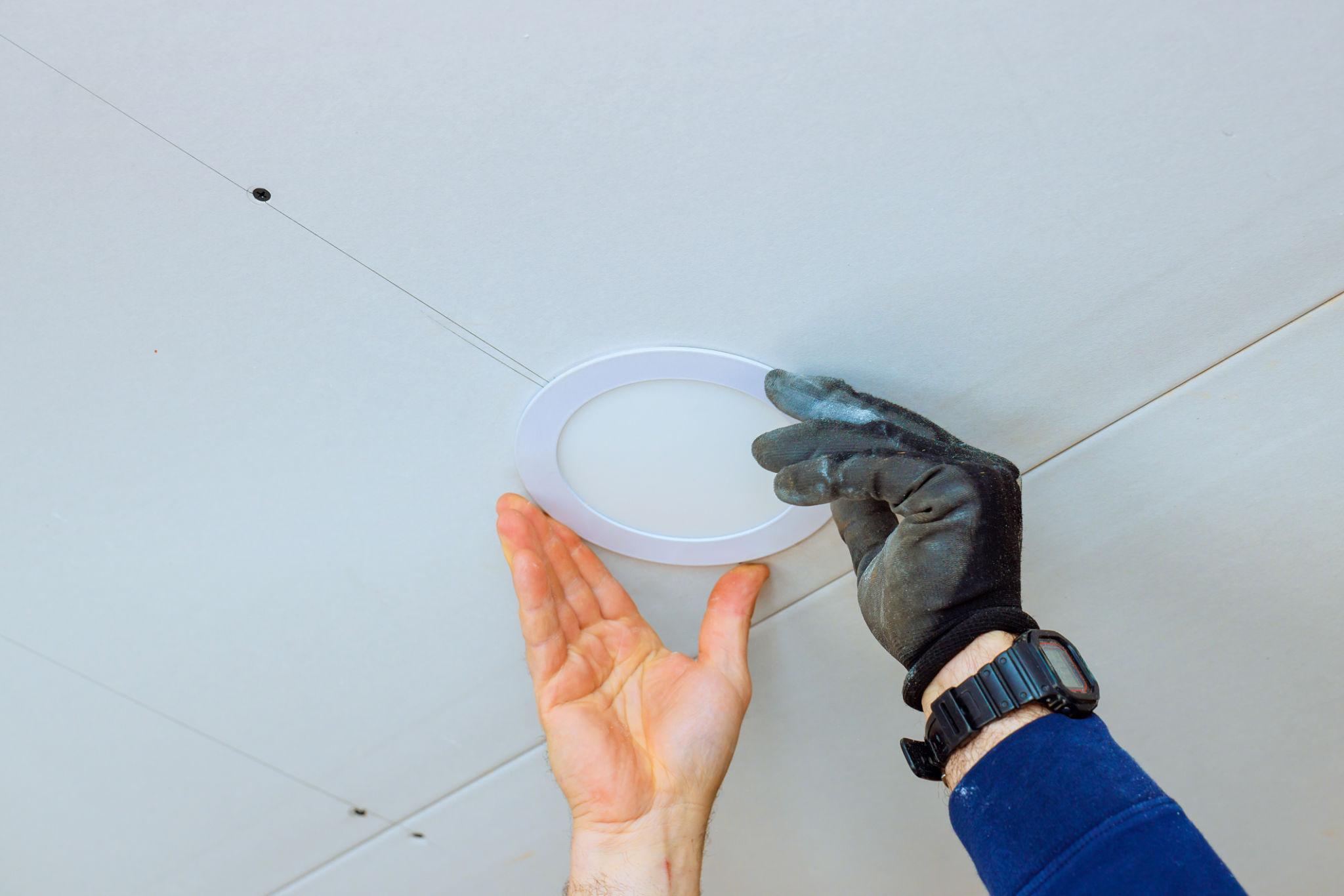 Electrician installing round recessed LED ceiling light during residential lighting upgrade.