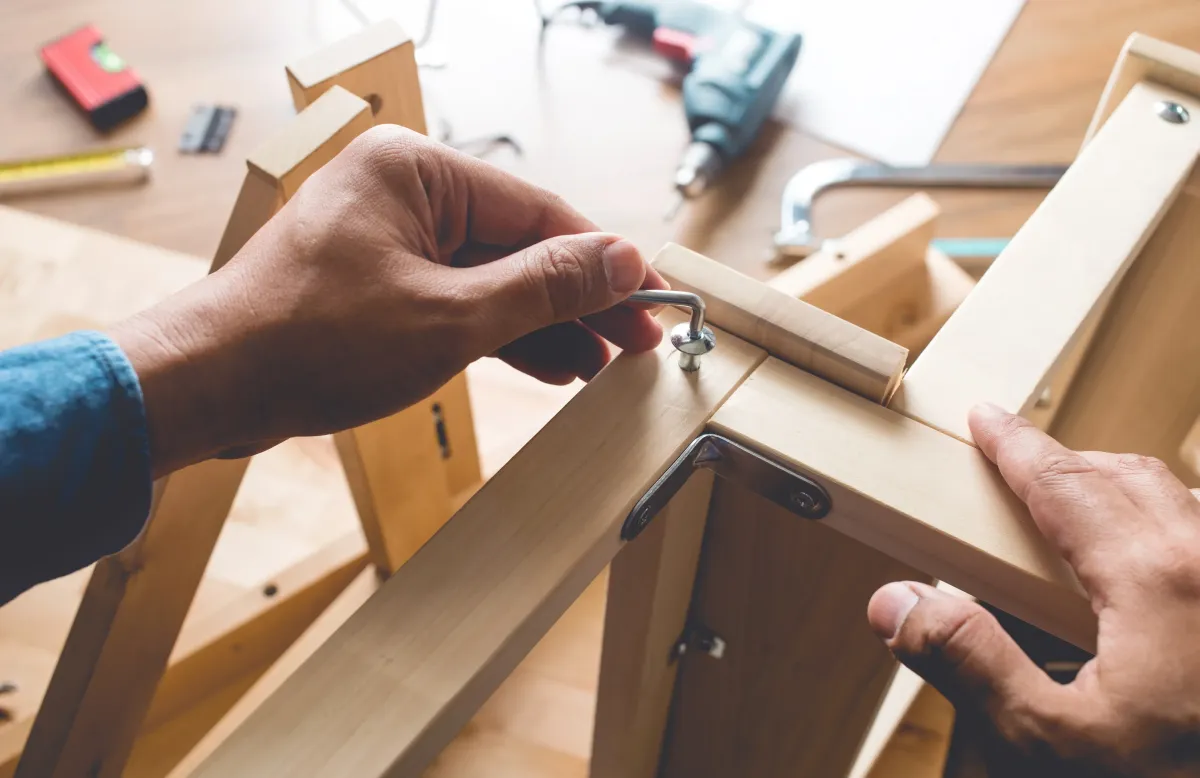 Hands assembling wooden furniture using Allen key during DIY furniture assembly project.