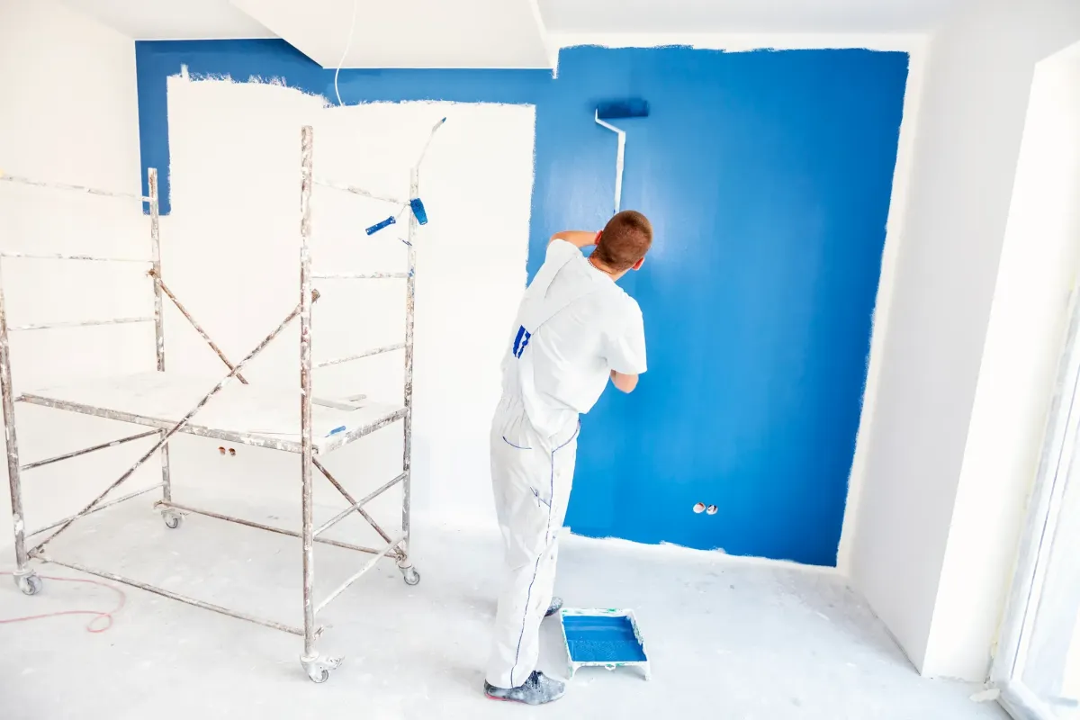 Professional painter using roller to paint interior wall blue during residential home renovation.