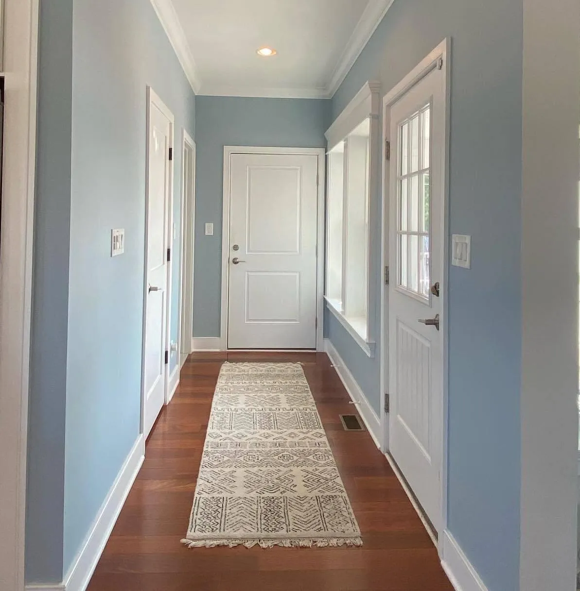 Bright hallway interior with light blue walls, white trim, hardwood floors, and front entry door.