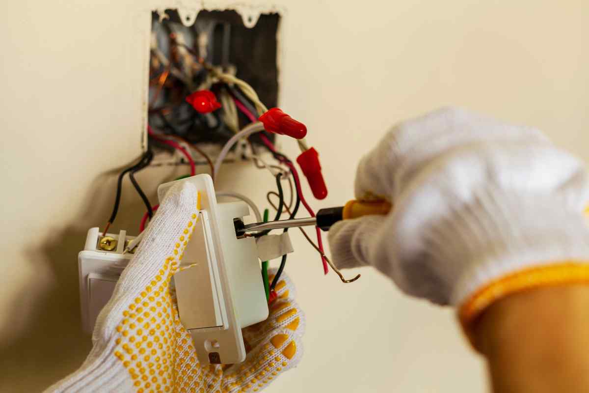 Electrician wiring a wall light switch using screwdriver during residential electrical repair.