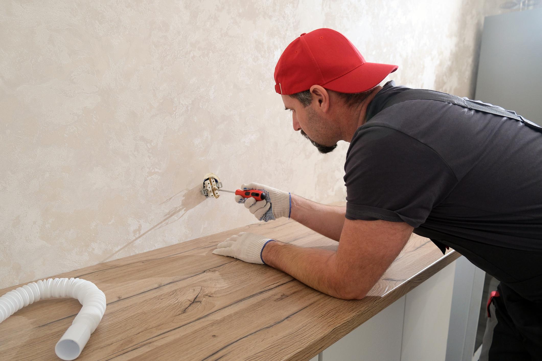 Electrician installing a wall outlet, tightening electrical wiring with a screwdriver during home repair.