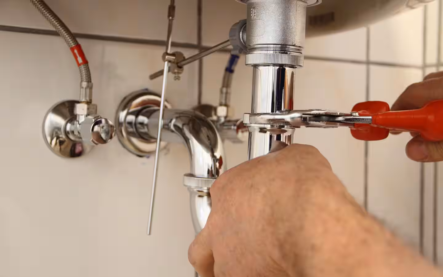 Plumber tightening sink drain pipe with wrench under bathroom sink