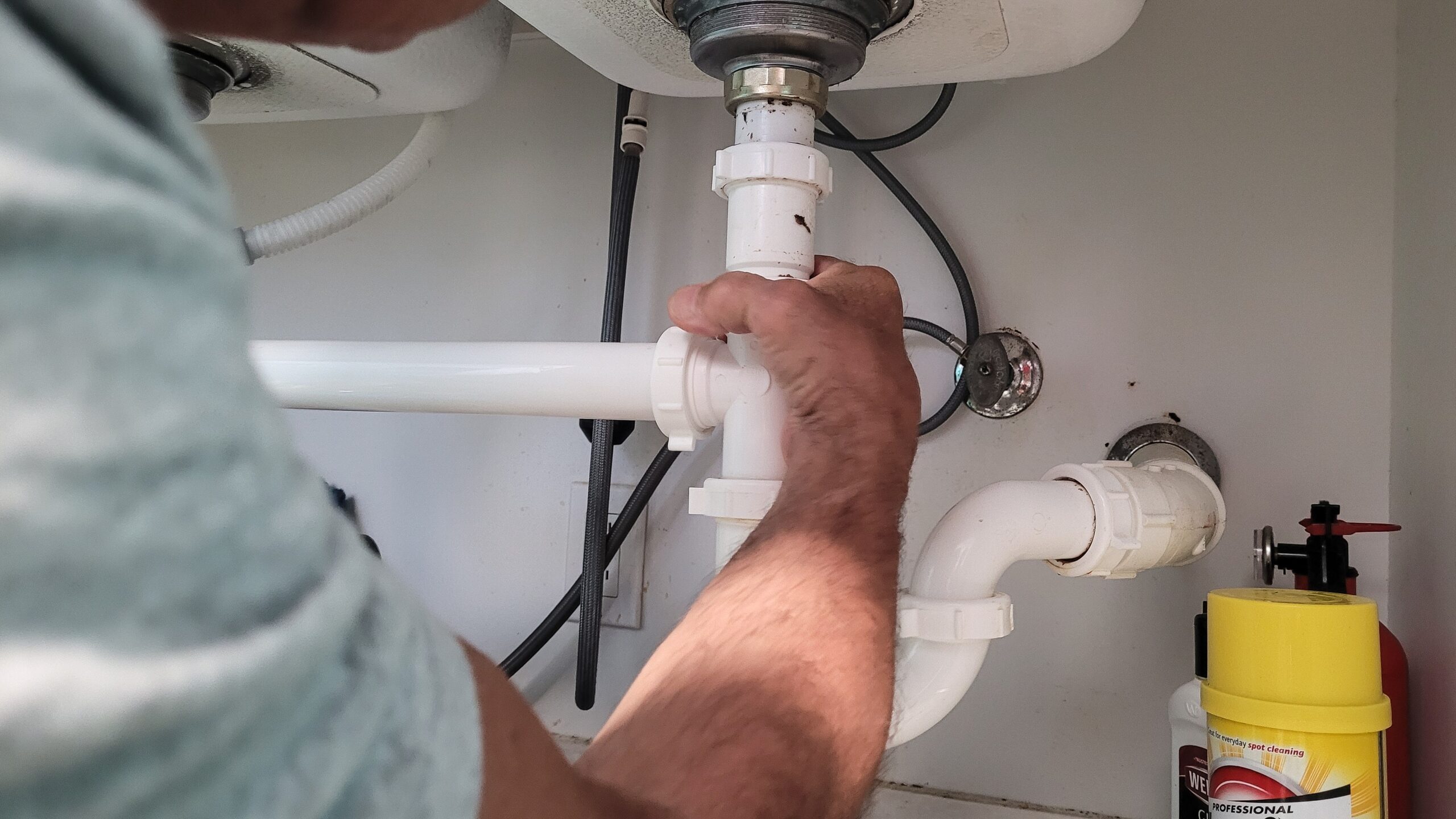 Plumber repairing under-sink drain pipe and P-trap connection for a kitchen sink plumbing fix.