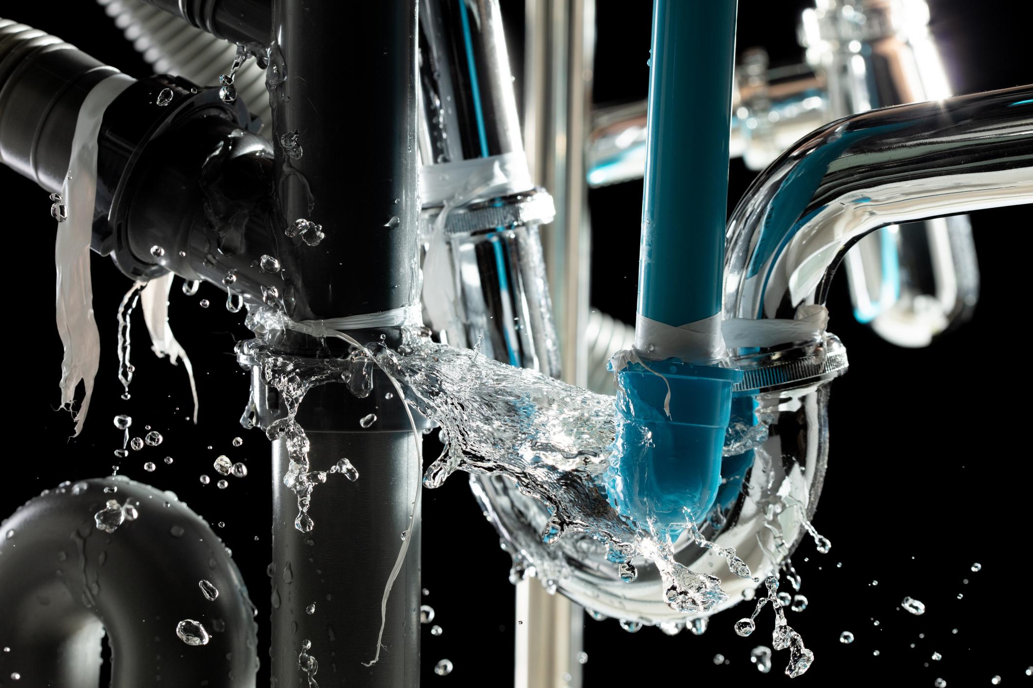 Burst pipe under sink spraying water from a leaking plumbing connection, emergency plumbing repair