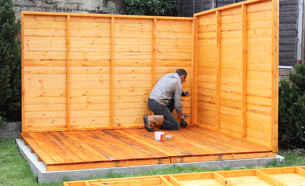 Contractor assembling wooden garden shed with pressure-treated lumber during backyard construction project.