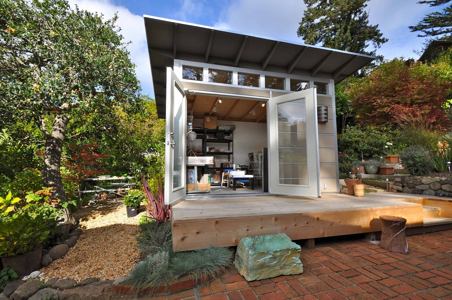 Modern backyard studio shed with double doors and wooden deck in landscaped garden