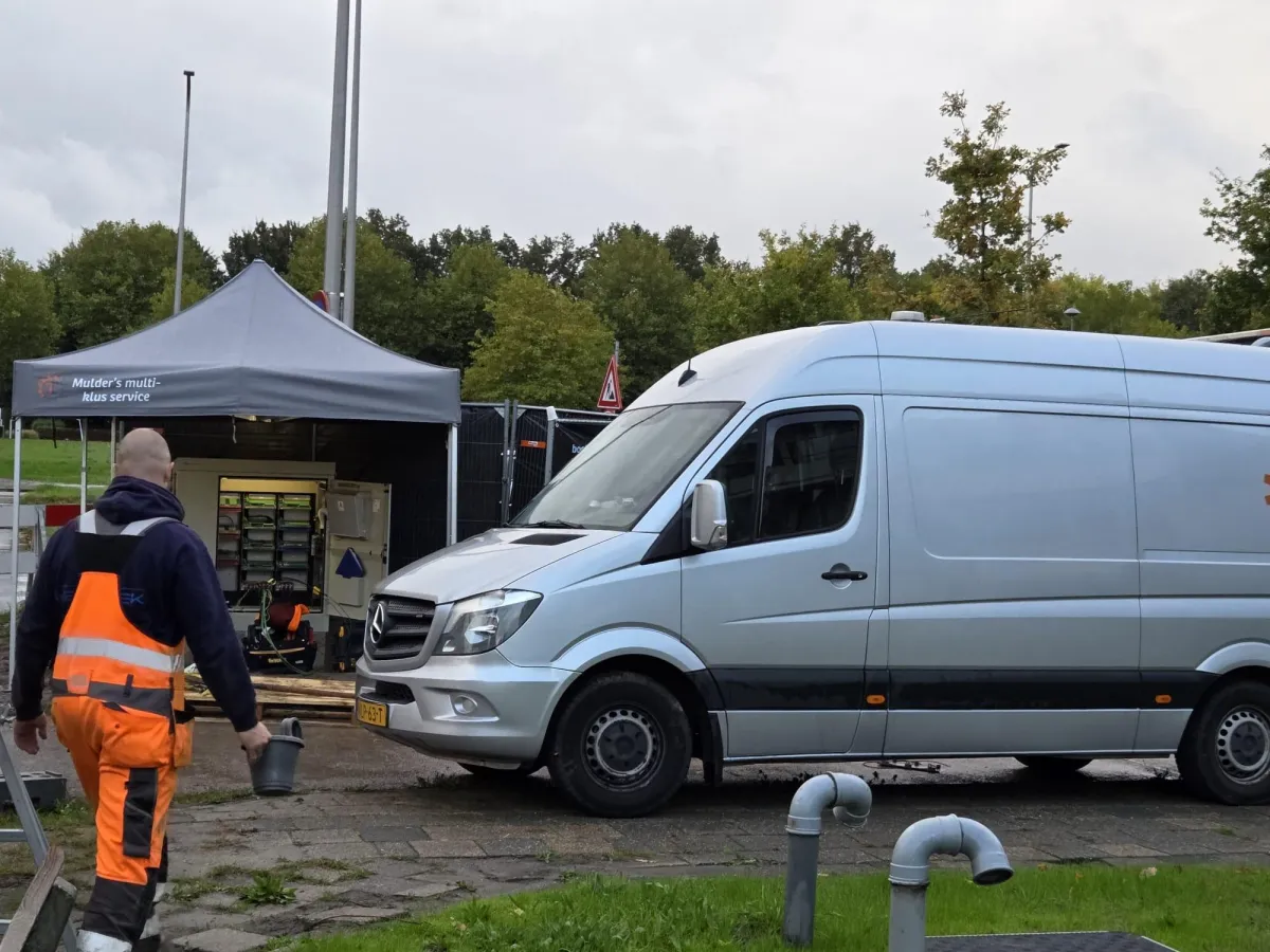 Ervaren vakman van Mulder's Multi Klus Service in werkkleding op locatie met naast hem de bus van Mulder's Multi-Klus service. De sfeer is professioneel en vriendelijk.