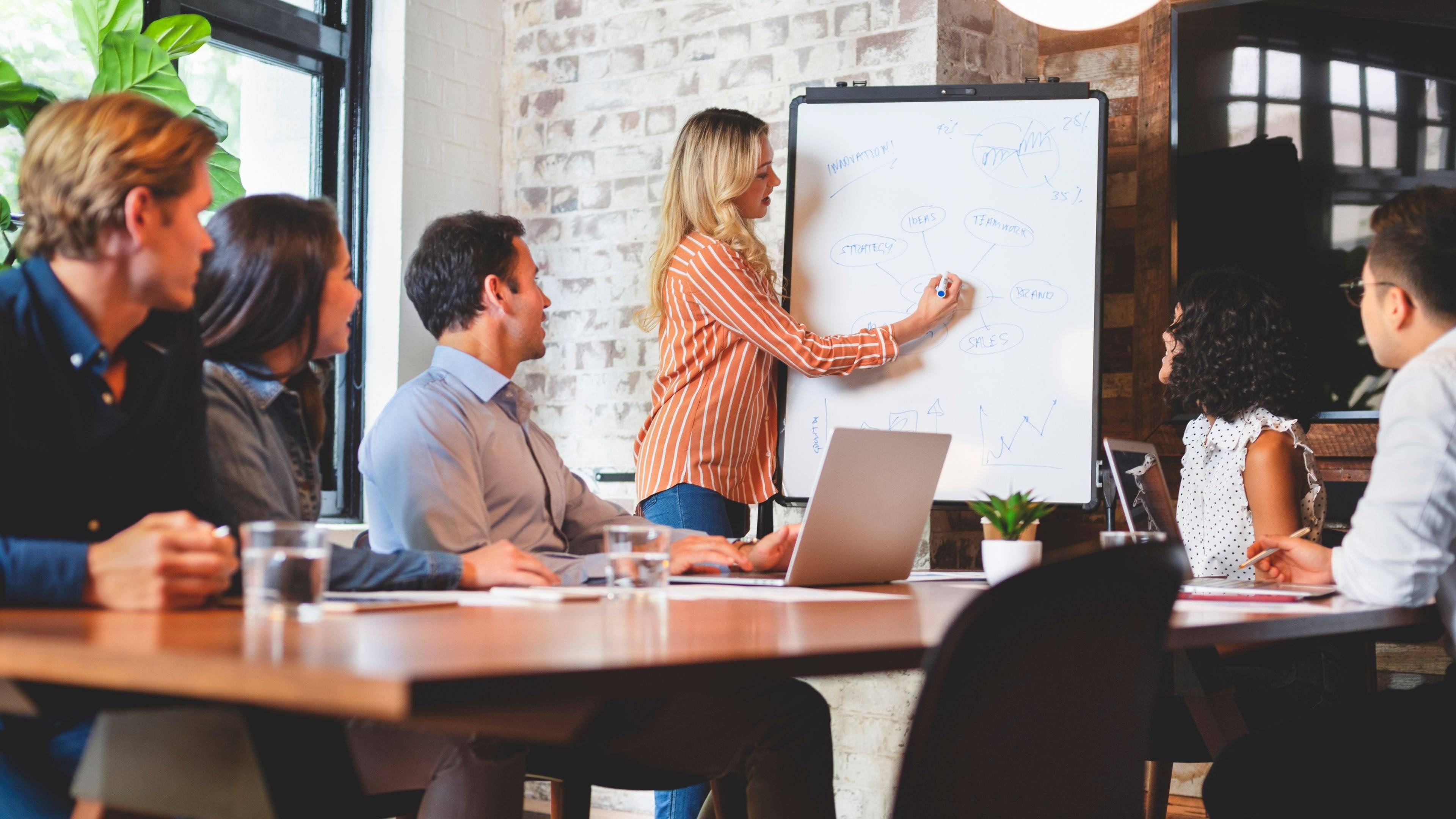 Team engaged in a leadership workshop while a facilitator presents strategy notes on a whiteboard, used by ALC People Solutions.